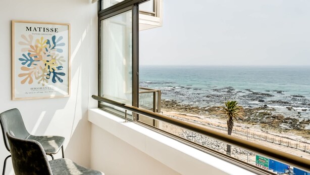 Ein Zimmer mit großem Fenster mit Blick auf einen felsigen Strand und den Ozean.