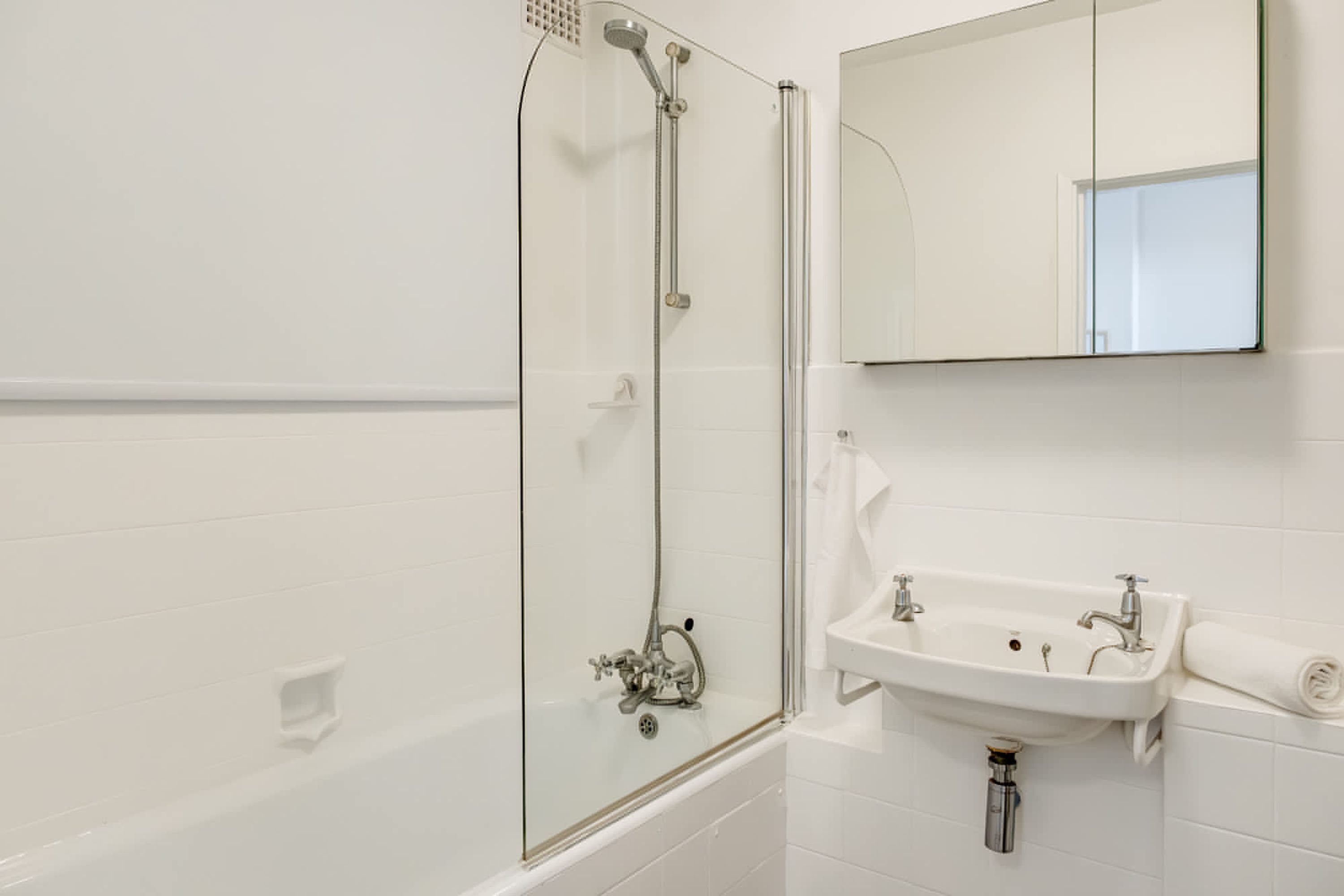 A bathroom with a glass-enclosed shower, a sink, and a mirror.