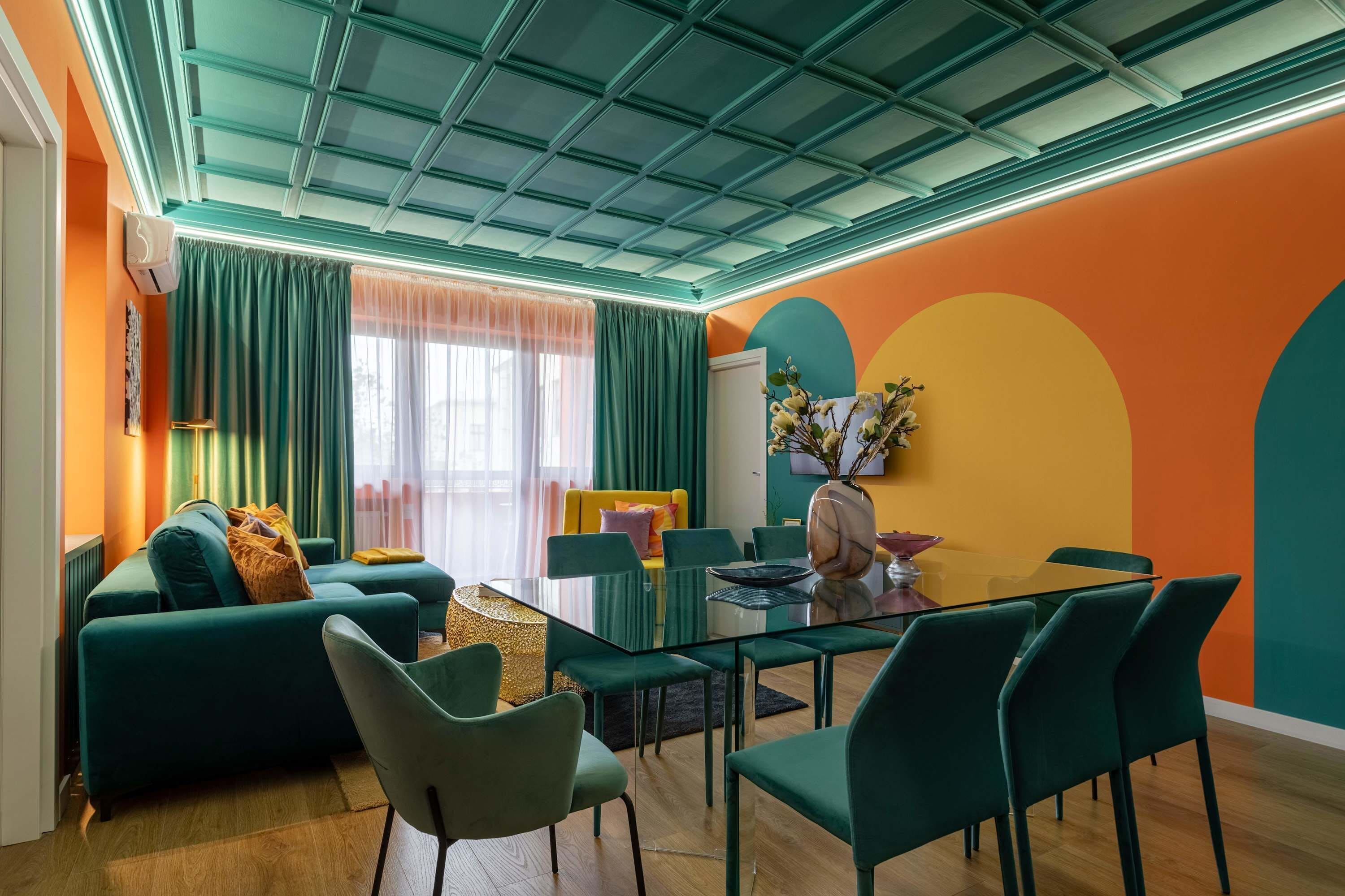 Un saló modern amb una taula de dinar de vidre, sofàs color turquesa i una paret d'accent taronja vibrant.