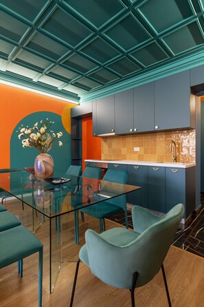 A modern kitchen with teal cabinetry, a glass dining table, and a vase with flowers.