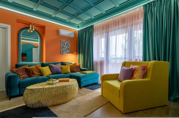 A modern living room with teal and yellow sofas, a textured coffee table, and a large window with sheer curtains.