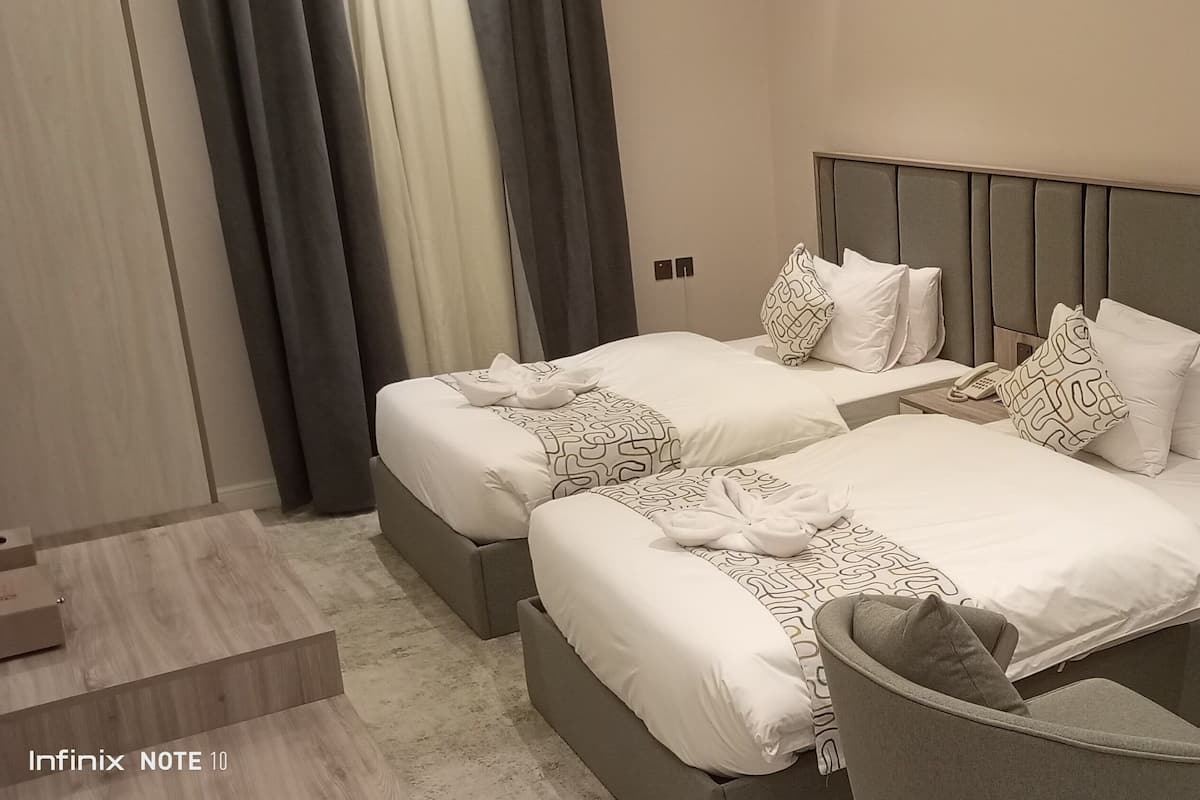 Camera d'albergo con due letti, un divano, un piccolo tavolino con un vaso e vista sull'esterno.