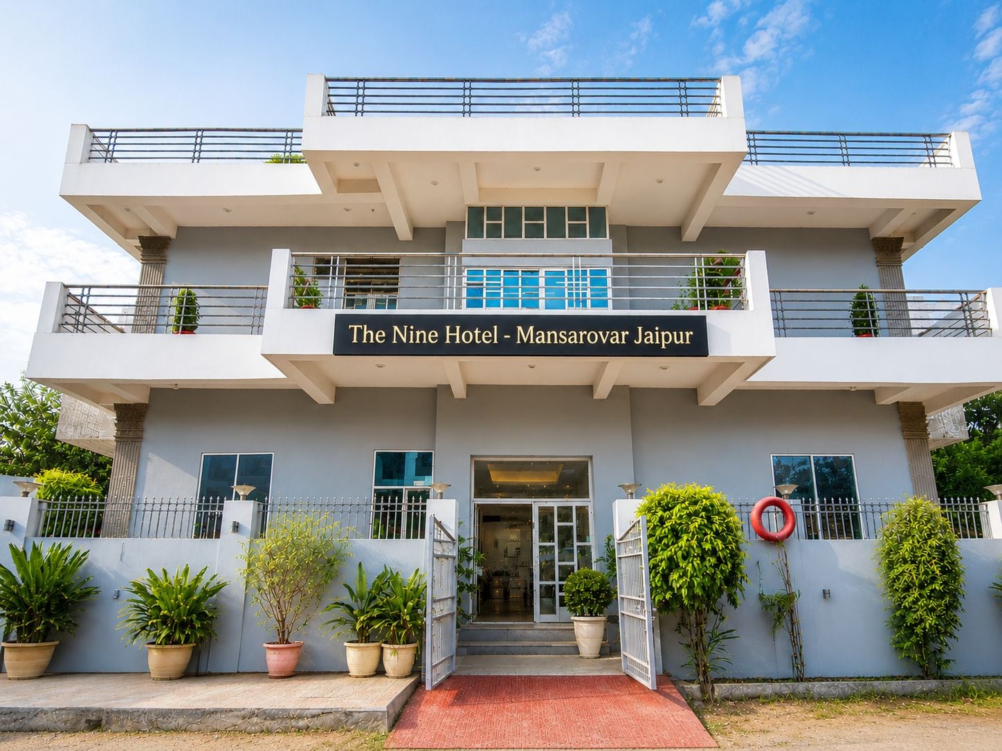 Un hotel moderno con una estructura de dos pisos, una entrada destacada y un letrero que indica que es 'The Nine Hotel - Mansarovar Jaipur'.