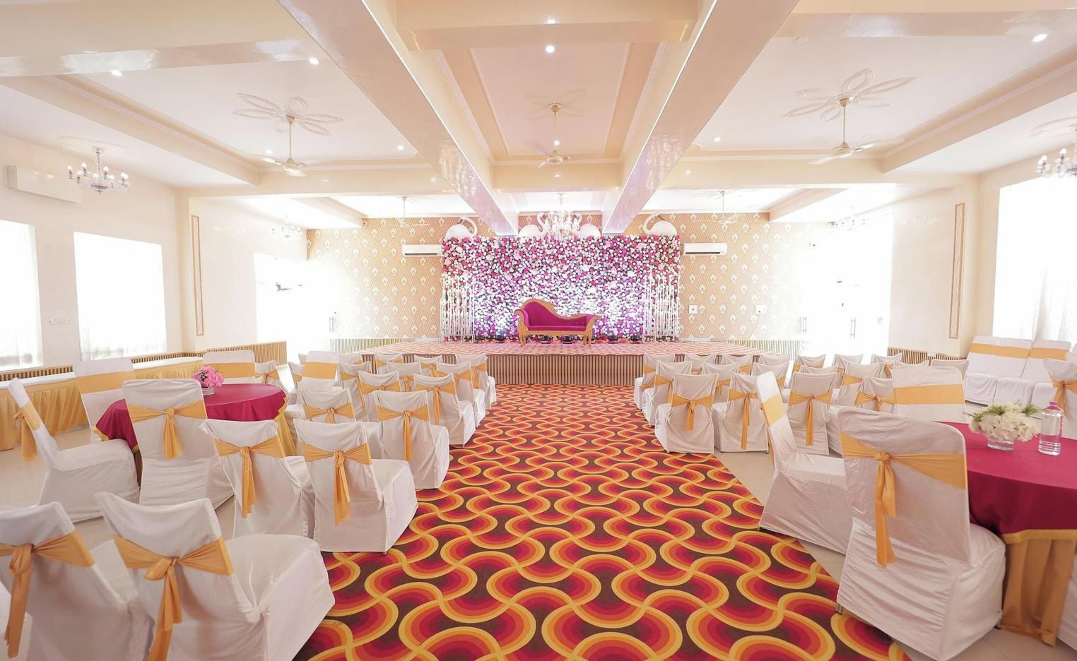 A banquet hall with rows of chairs, a stage with a pink sofa, and a floral backdrop.