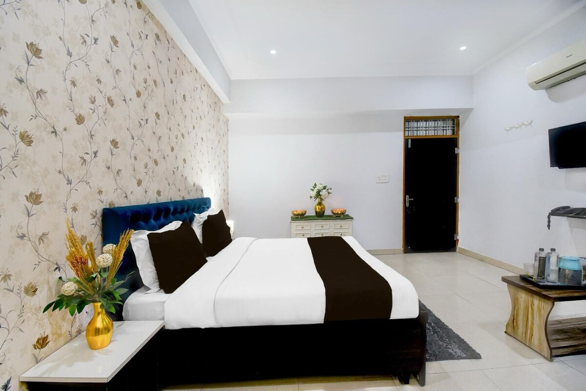 A modern bedroom with a large bed, a nightstand, a dresser, a TV, and a door leading to another room.