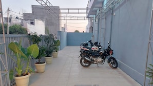 Une ruelle étroite, avec une moto garée sur le côté droit, des plantes en pot sur le côté gauche et un portail métallique au fond.