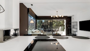 A modern kitchen with a built-in Bosch induction cooktop, a large window offering a view of the outdoors, and a minimalist design with a flat-screen TV mounted on the wall. - Dunes Paradise Suite (Marbella)