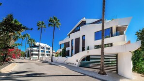 A modern building with a unique curved facade, palm trees, and a clear blue sky. - Dunes Paradise Suite (Marbella)