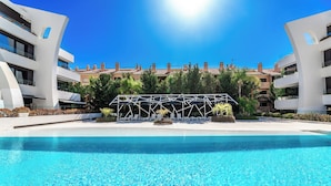 A swimming pool with a clear blue water surface, surrounded by modern buildings with balconies and a covered outdoor seating area. - Dunes Paradise Suite (Marbella)