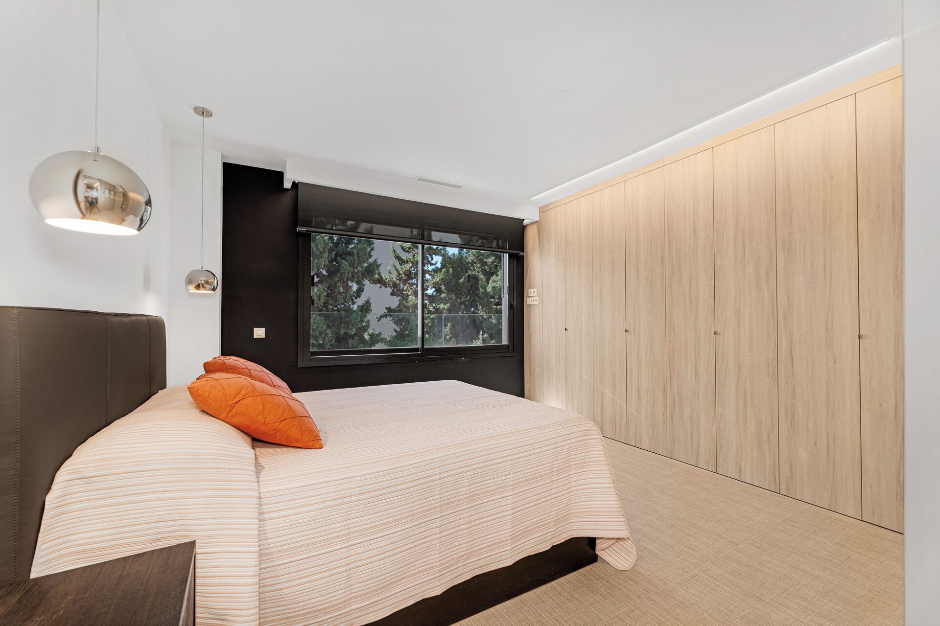 Ein modernes Schlafzimmer mit einem Bett, einem Fenster mit Blick auf Bäume und einem Kleiderschrank.