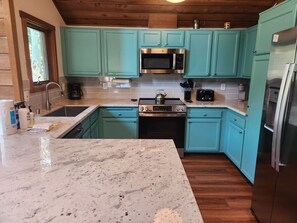 Una cocina con gabinetes color turquesa, un microondas de acero inoxidable, una estufa y un refrigerador.