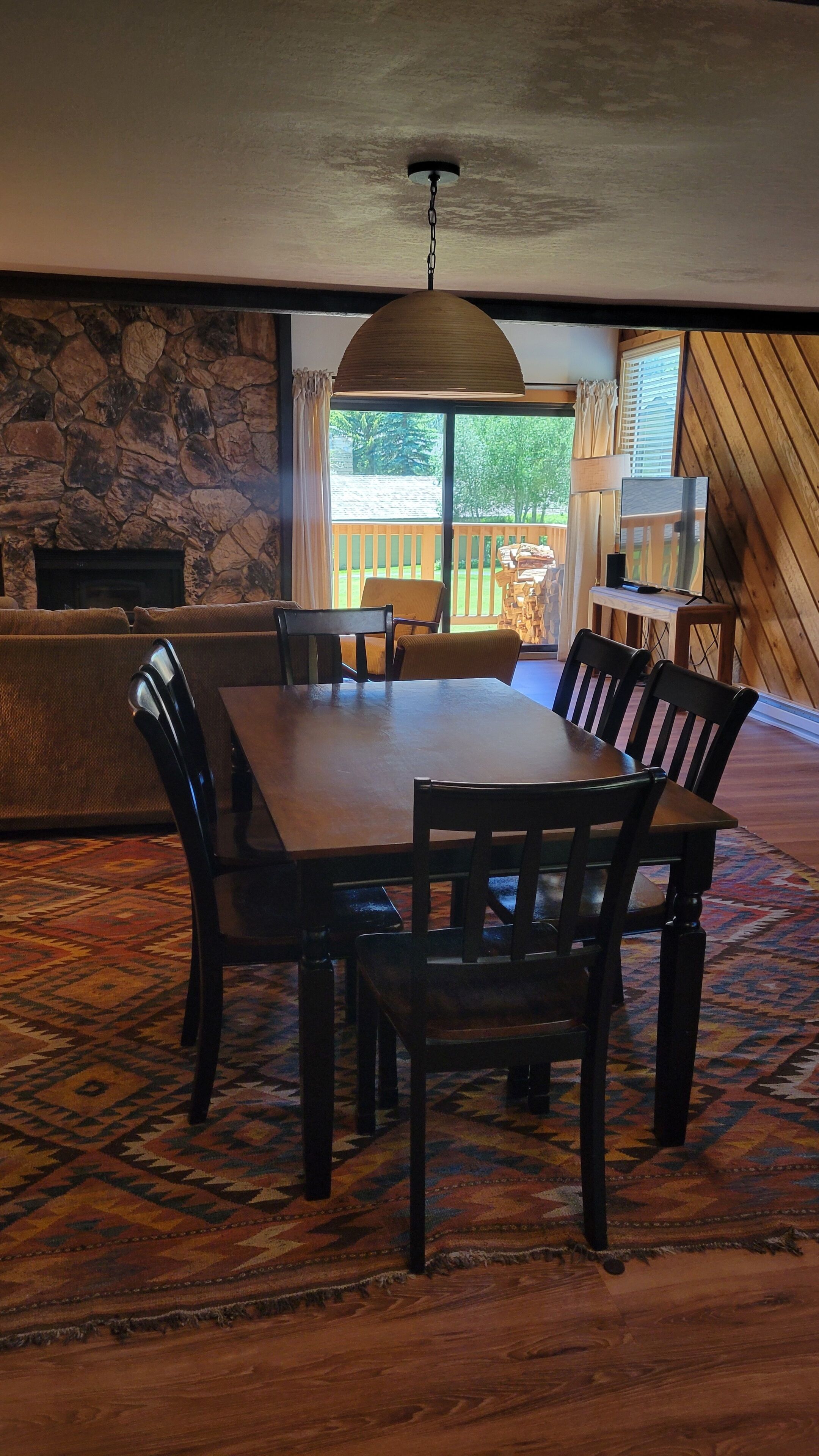 Un espace repas avec une grande table et des chaises en bois, un mur en pierre et une vue sur l’extérieur.