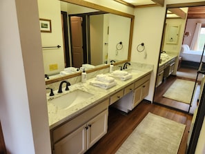 A hotel bathroom with a large mirror, two sinks, and a wooden floor.