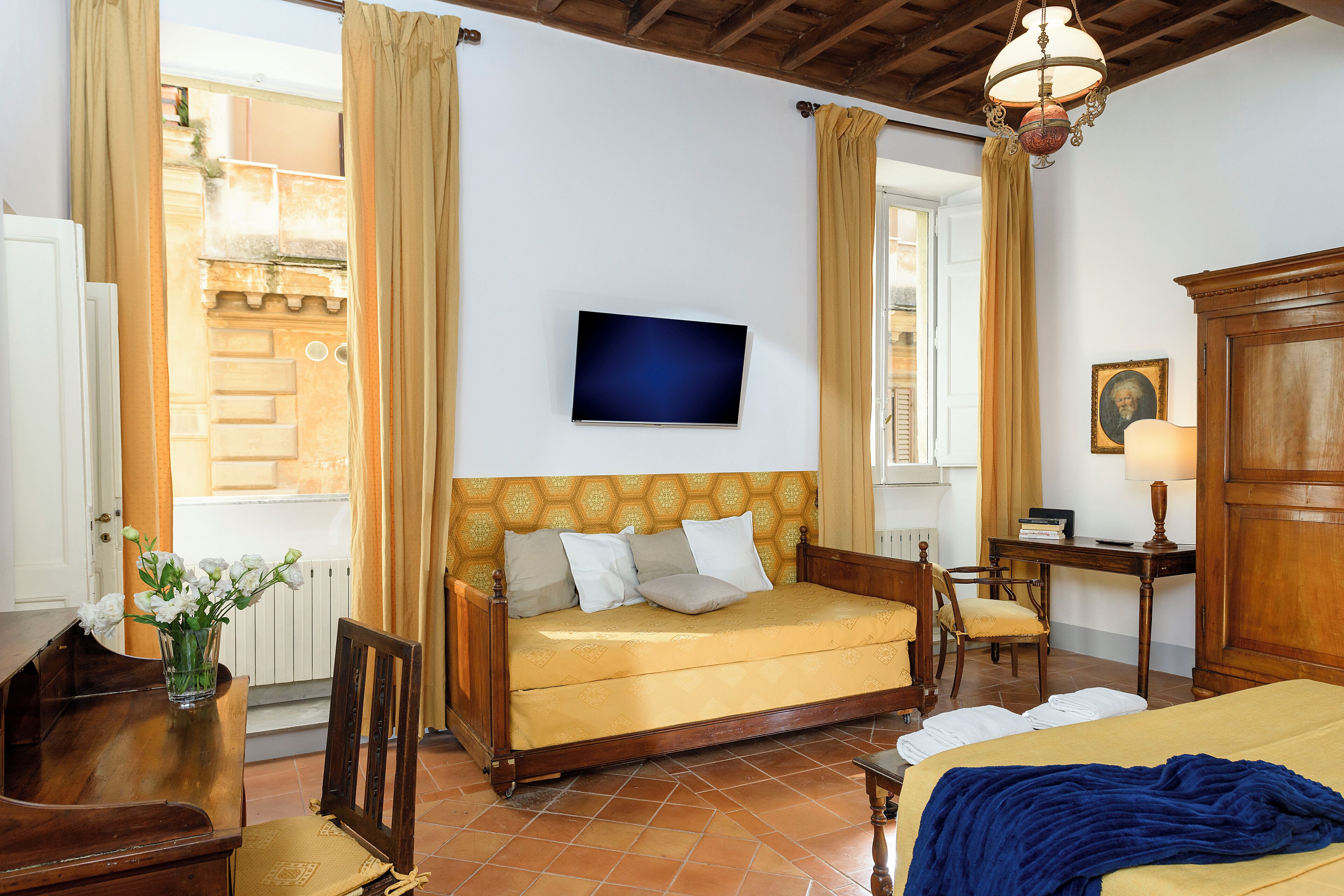 Quarto com sofá de madeira, televisão na parede, escrivaninha com cadeira e cama com manta azul.