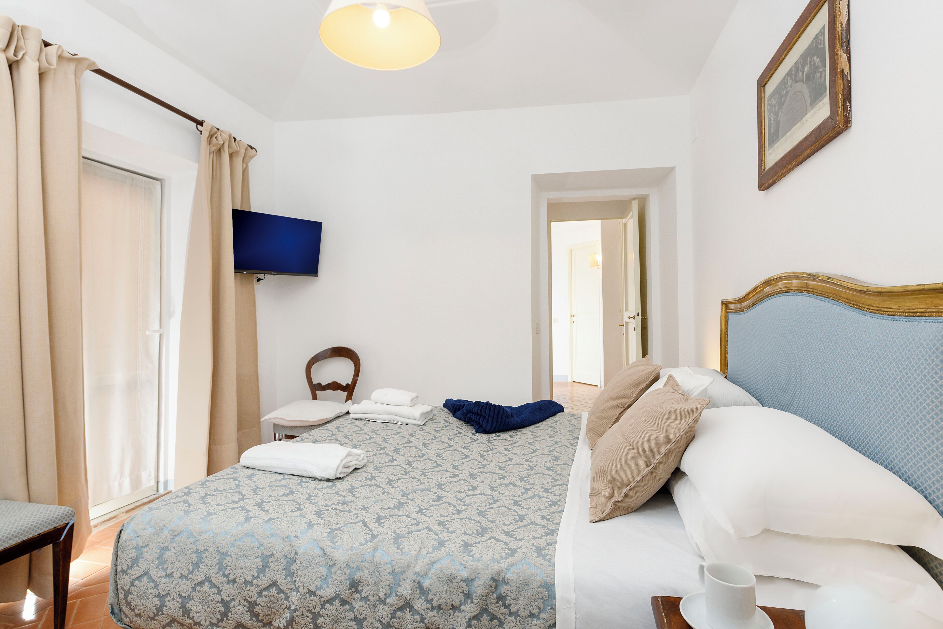 A hotel room with a bed, a chair, a TV, and a door leading to another room.