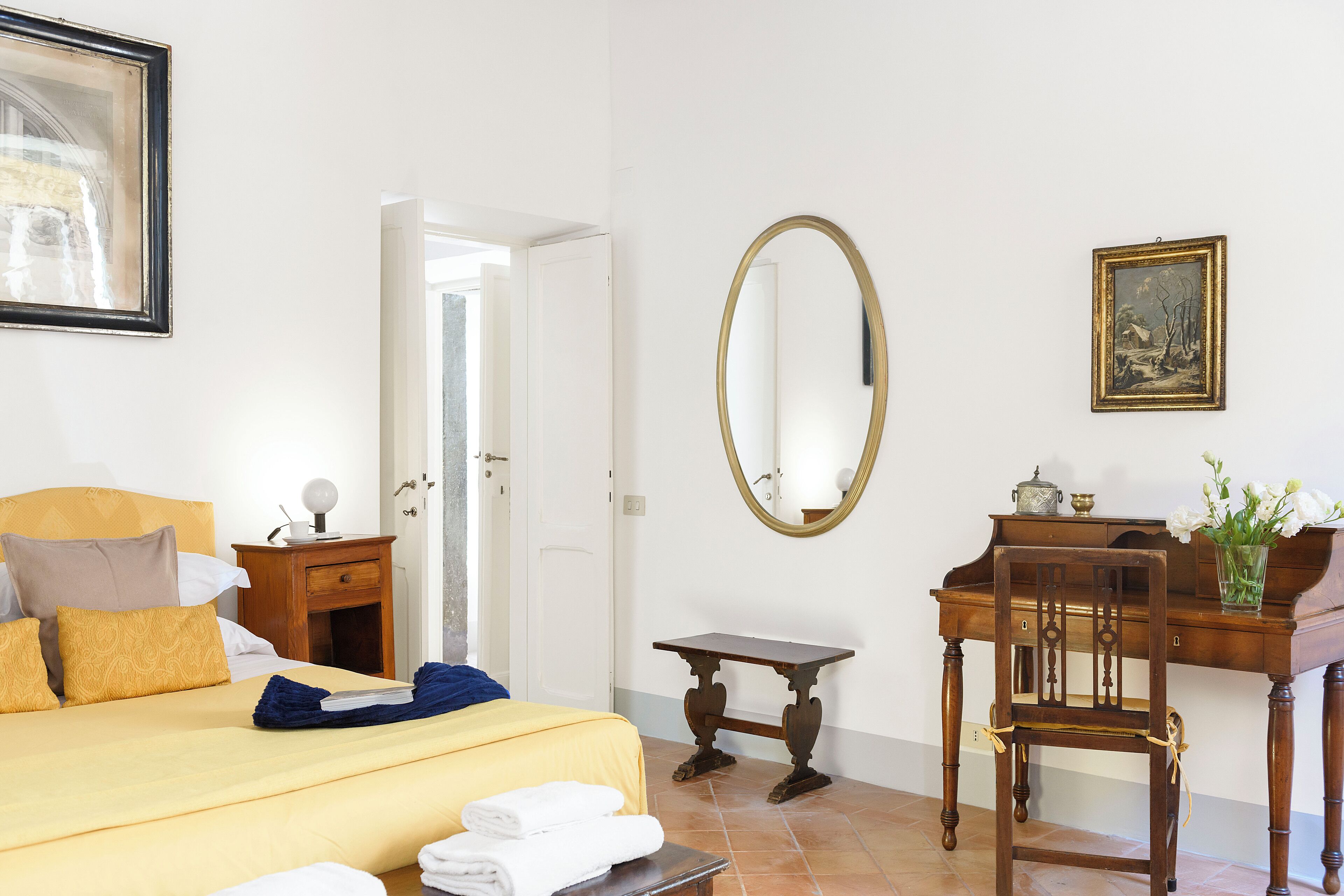 Hotellihuone, jossa on sänky, puinen työpöytä, tuoli, peili ja taulu seinällä.