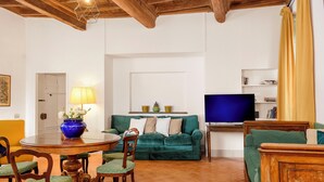 A living room with a green sofa, wooden chairs, a dining table, a TV, and a lamp. - Cartari Deluxe Apartment (Rome)