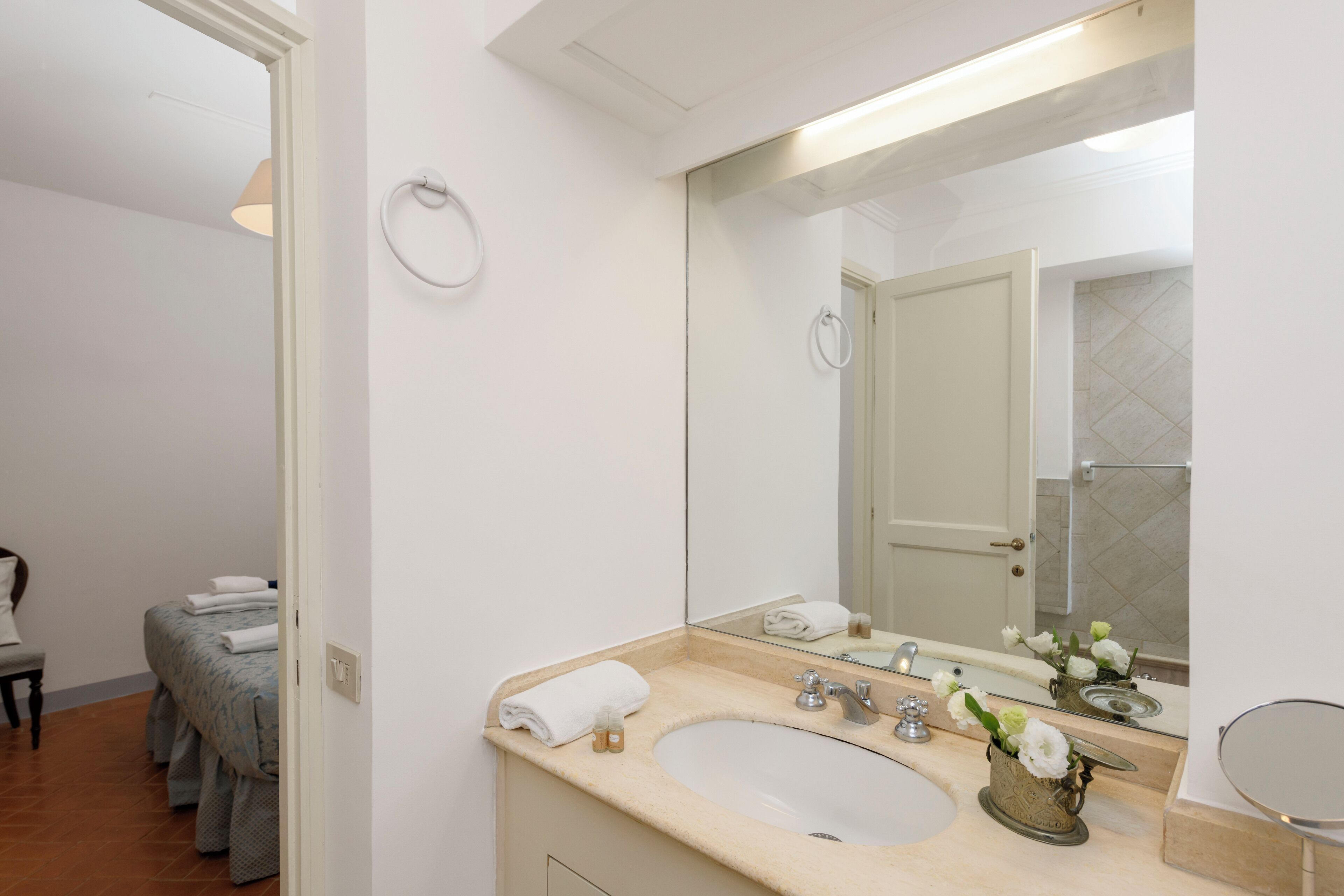 A bathroom with a sink, mirror, towel ring, and a shower area visible in the background.