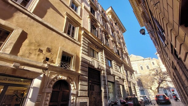 A street view with a barber shop on the left, a building with a balcony, and parked cars. - Cartari Deluxe Apartment (Rome)