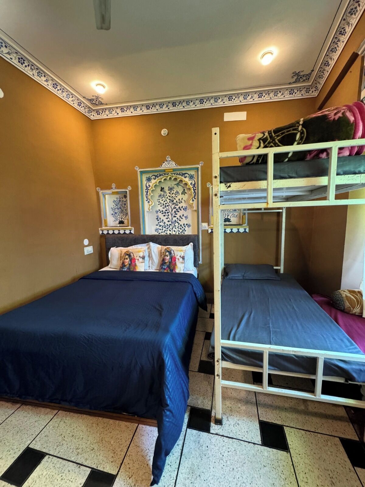 A dormitory room with two bunk beds, a decorative wall panel, and a small bedside table.