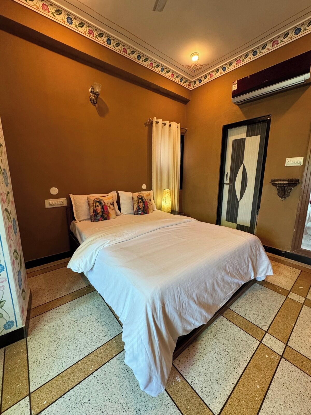 Une chambre d’hôtel avec un grand lit, une table de chevet, un climatiseur fixé au mur et un décor de moulure ornant le plafond.