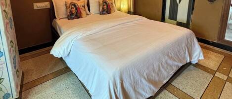 A hotel room with a large bed, a nightstand, a wall-mounted air conditioner, and a decorative ceiling border.