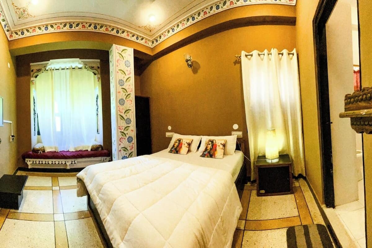 Camera d'albergo con un letto grande, una televisione, un comodino con una lampada e un pannello decorativo a parete.