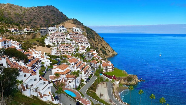 A coastal town with white buildings, a swimming pool, and a view of the ocean.