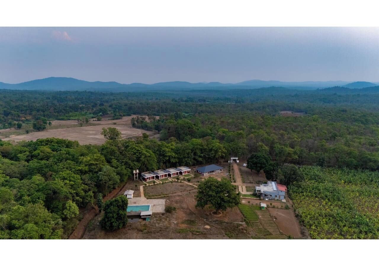 Vista aérea de una propiedad rural con varias edificaciones, rodeada de un bosque denso y campos abiertos.