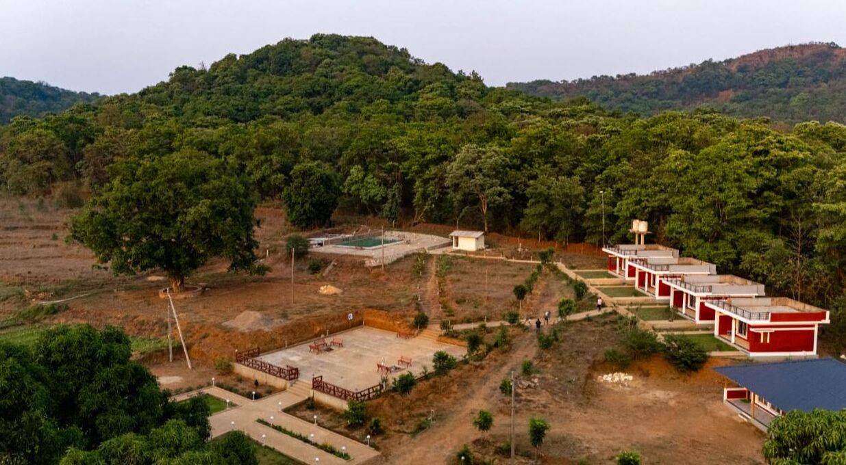 A hotel with a row of red buildings, a swimming pool, and a hilly backdrop.