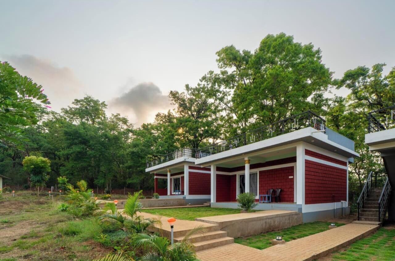 A two-story building with a red and white exterior, surrounded by lush greenery and trees.