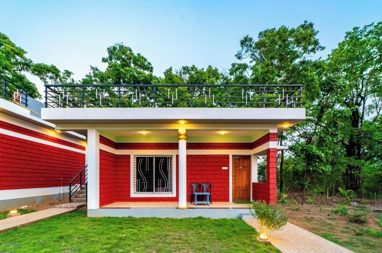 A two-story building with a red exterior, a balcony on the upper floor, and a small porch area with a chair.