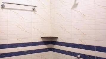 Ducha en esquina con cabezal de ducha de mano, toallero y lavamanos en esquina.