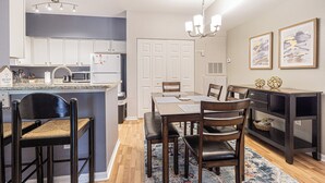A modern kitchen with white cabinets, a built-in microwave, and a dining area with a wooden table and chairs.