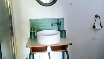 Um banheiro com pia branca, painel de azulejos verdes e espelho redondo.