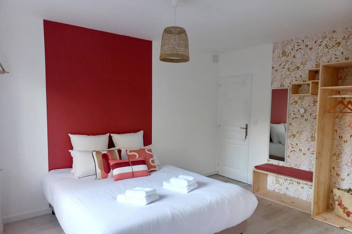A bedroom with a bed, pillows, a hanging light, a wardrobe, and a door.