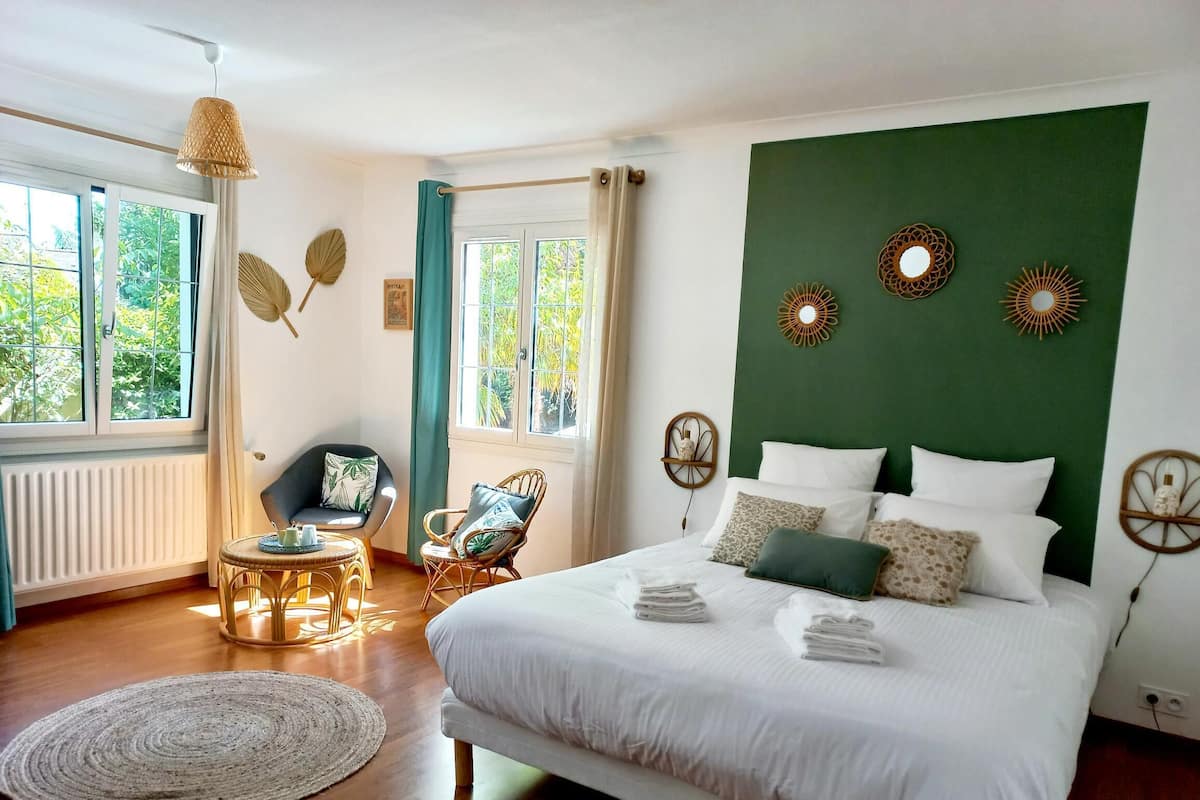 A bedroom with a large bed, two chairs, a small table, and a window with curtains.