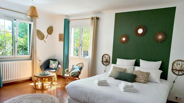 A bedroom with a large bed, two chairs, a small table, and a window with curtains. - Le Clos Beauséjour (Mauges-sur-Loire)