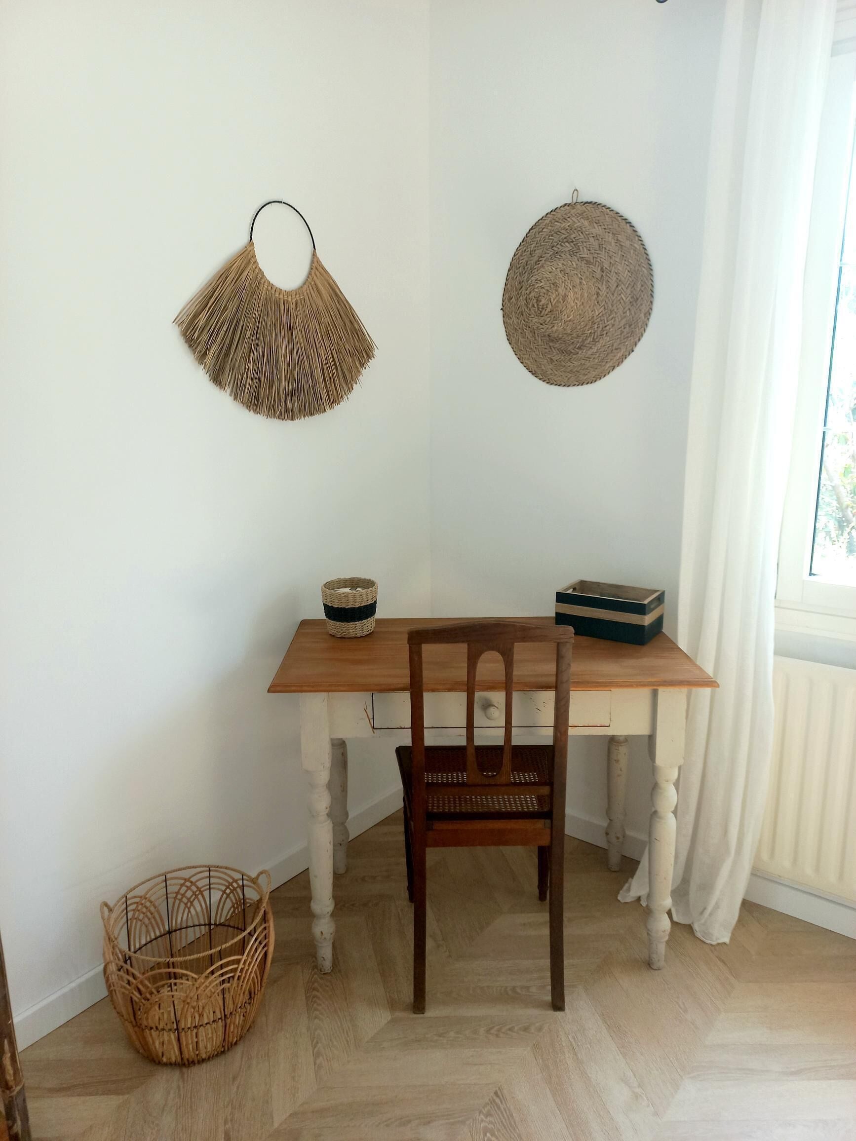 Una mesa de comedor de madera con una silla tejida, dos adornos tejidos en la pared y una cesta tejida en el suelo.