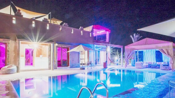 Ein Poolbereich bei Nacht mit klarem Wasser, Liegestühlen und Sonnenschirmen.