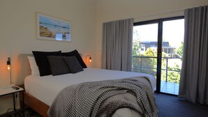 Habitación de hotel con una cama grande, una mesita de noche con una lámpara, un cuadro en la pared y vistas al exterior a través de una puerta corredera.