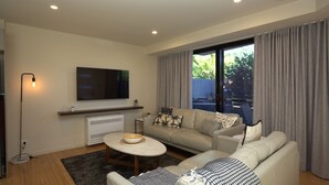 Una sala de estar moderna con sofá, mesa de centro, televisor de pantalla plana y un ventanal con cortinas.