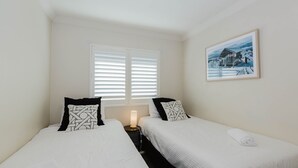 Un dormitorio con dos camas, ropa de cama blanca, almohadas estampadas en blanco y negro, una lámpara de noche y un cuadro en la pared.