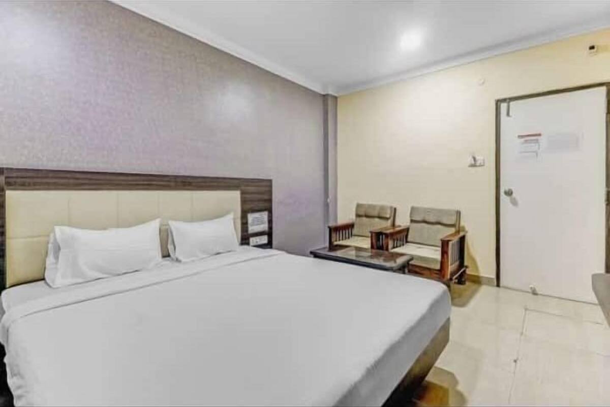 Ein Hotelzimmer mit einem großen Bett, zwei Nachttischen, einem Sessel und einer Tür.