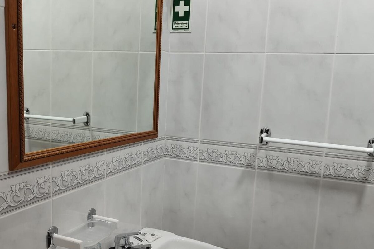 A bathroom with a white sink, a mirror, and a handrail.