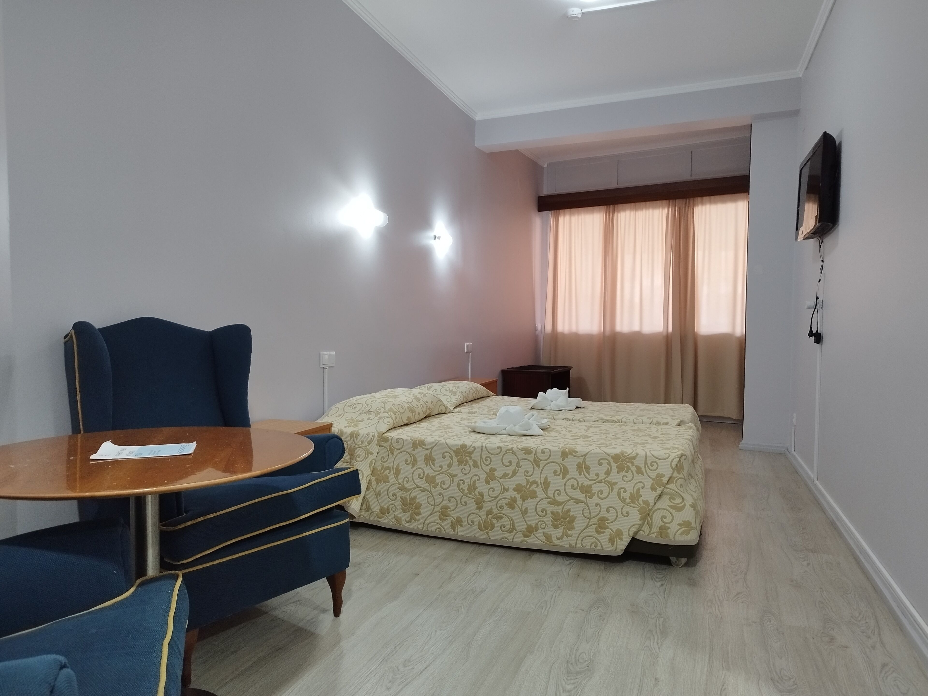 Een hotelkamer met een bed, een bureau met stoel, een televisie en een raam met gordijnen.