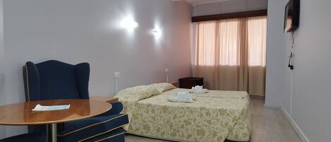 A hotel room with a bed, a desk with a chair, a TV, and a window with curtains.