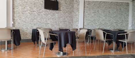 Un salón de conferencias con pared de ladrillo, un televisor de pantalla plana montado y varias mesas con sillas.