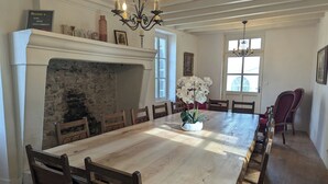 Un comedor con una gran mesa de madera, sillas, chimenea y una araña.