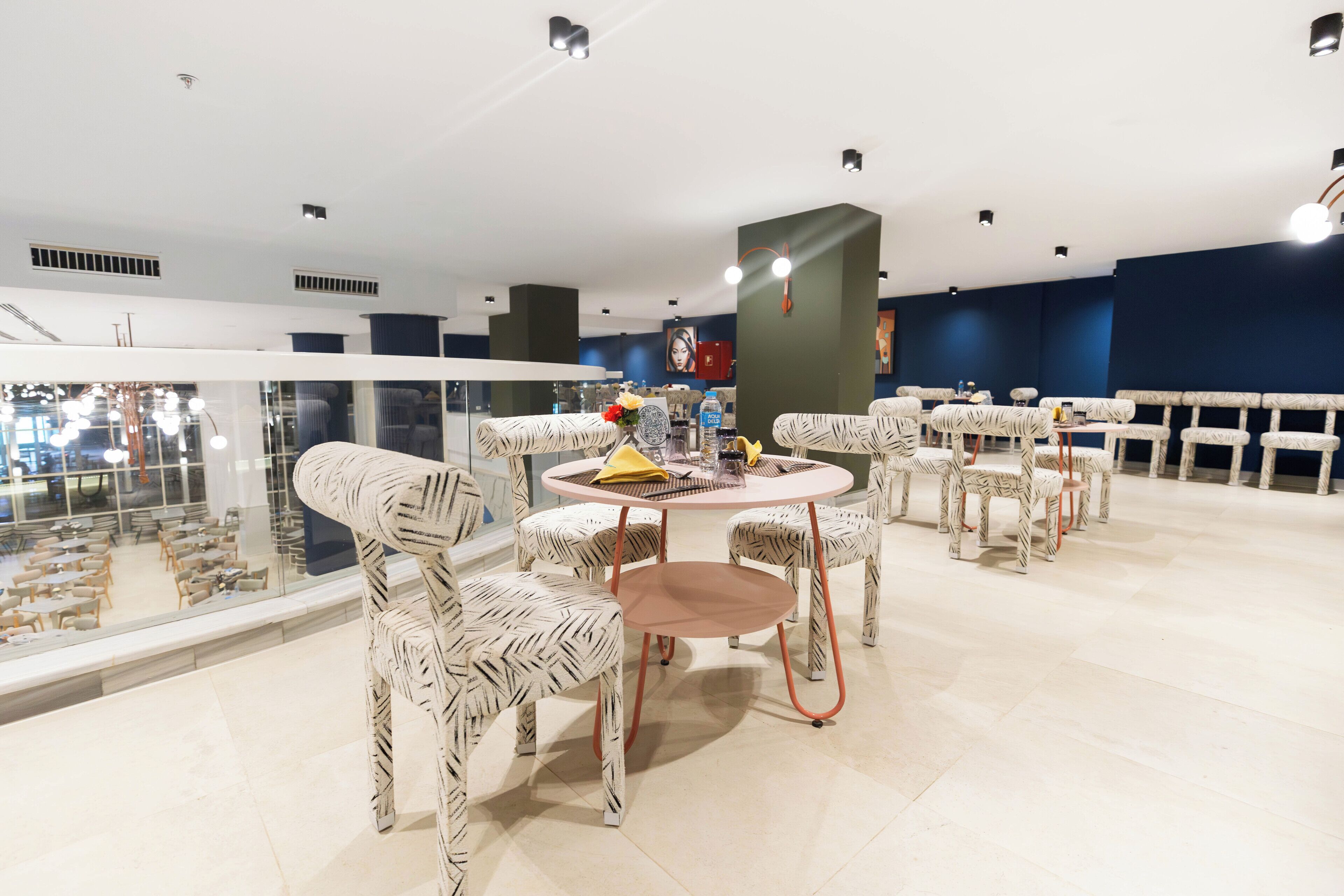 A modern dining area with round tables and zebra-striped chairs, a glass railing, and a view of the dining hall below.